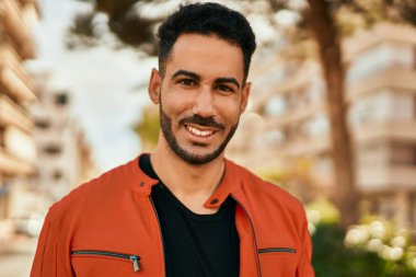 Genç İspanyol adam gülümseyerek şehirde mutlu mesut dikiliyor..