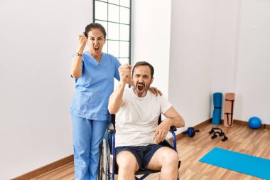 Tekerlekli sandalyede oturan İspanyol orta yaşlı bir adam ve rehabilitasyon kliniğindeki hemşire öfkeyle bağırıyor, öfkeyle bağırıyor ve el kaldırıyor. 