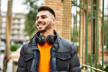 Sakallı yakışıklı, neşeli ve kendine güvenen, kışlık palto ve kulaklık takan bir İspanyol.