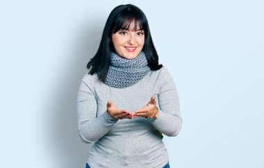 Kış eşarbı takan, elleri avuçlarında gülümseyen, el hareketi yapan, genç, Latin kökenli bir kadın. Bekleme ve koruma 