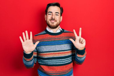Sakallı, zarif yün süveter giyen yakışıklı beyaz adam sekiz numarayı gösterip parmaklarını gösterirken kendinden emin ve mutlu gülümsüyor.. 
