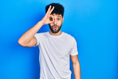 Sakallı, sıradan beyaz tişörtlü genç bir Arap. Şaşırmış yüz ifadesiyle şaşırmış, parmaklarından bakan bir jest yapıyor. İnançsız ifade. 