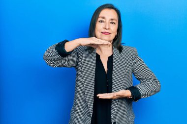 Orta yaşlı İspanyol kadın iş kıyafetleri giyiyor. Ellerinde büyük ve büyük boy işareti var. Ölçü sembolü. Kameraya bakıp gülümsüyor. ölçüm kavramı. 