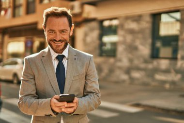 Şehirdeki akıllı telefondan gülümseyen orta yaşlı bir işadamı..