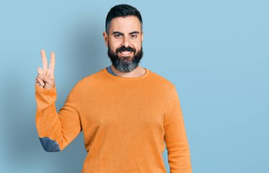 Sakallı, sıradan bir süveter giyen İspanyol bir adam iki numarayı gösterip gülümseyerek kendinden emin ve mutlu bir şekilde gülümsedi.. 