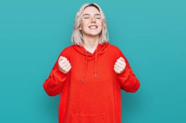 Başarı için heyecanlı, kolları havada ve gözleri kapalı, sıradan kıyafetler giyen genç sarışın kız zaferi kutlarken gülümsüyor. Kazanan konsept. 