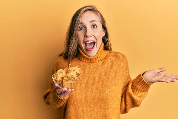 Mujer Rubia Joven Sosteniendo Tazón Con Pasta Cruda Celebrando Logro —  Fotos de Stock