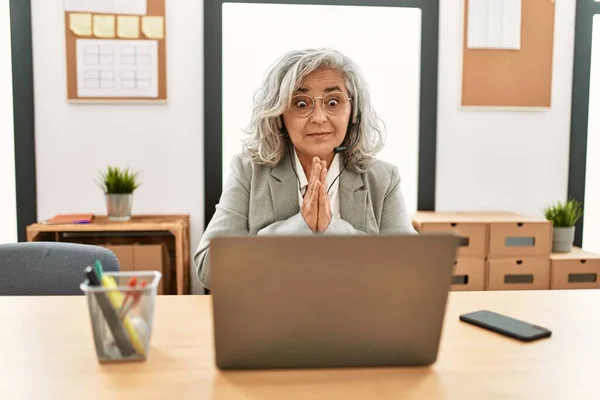 中年女商人坐在办公桌前 手拉手在办公室里用笔记本电脑祈祷 祈求宽恕 脸上带着自信的笑容 — 图库照片