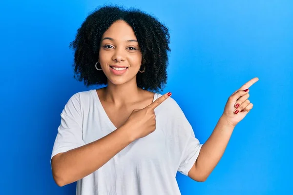 年轻的非洲裔美国女孩穿着随意的白色T恤 微笑着看着摄像机 用双手和手指指向旁边 — 图库照片