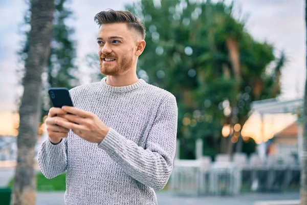 Beyaz adam şehirde akıllı telefon kullanarak mutlu bir şekilde gülümsüyor..