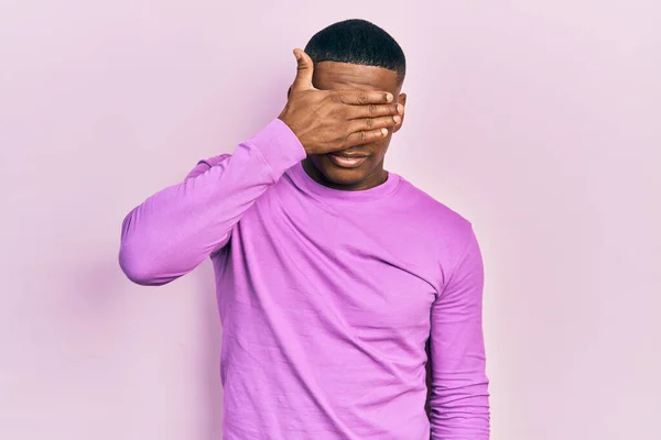 年轻的黑人男子穿着宽松的粉色毛衣 用手捂住眼睛 看起来严肃而忧郁 躲藏和拒绝的概念 — 图库照片