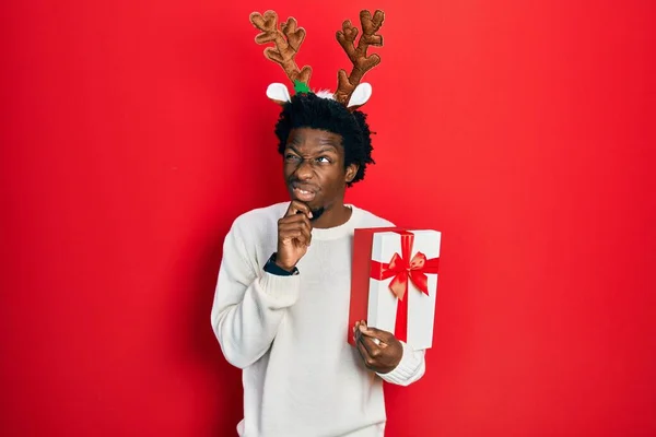 Jovem Afro Americano Vestindo Chapéu Natal Veado Segurando Presente Pensando — Fotografia de Stock