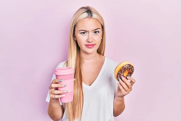 Menina Loira Jovem Comer Donut Beber Café Cético Nervoso Franzindo — Fotografia de Stock