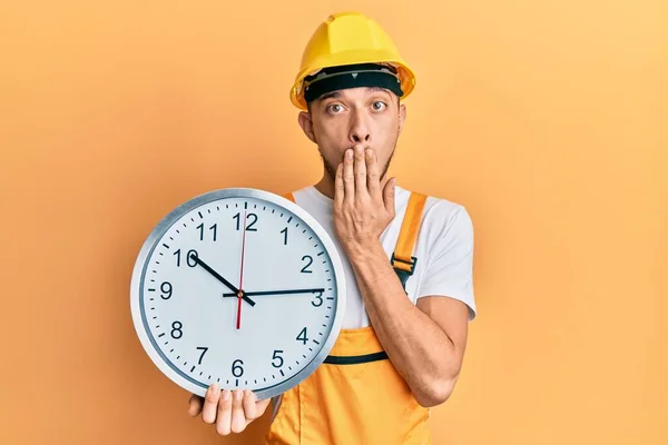 Joven Hispano Vistiendo Uniforme Constructor Sombrero Fuerza Sosteniendo Reloj Cubriendo — Foto de Stock