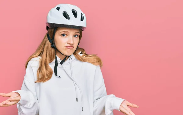 年轻美丽的高加索女孩戴着自行车头盔 毫无头绪 满脸困惑 手臂和双手高举 怀疑概念 — 图库照片