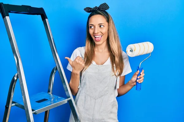 Hermosa Mujer Hispana Por Escaleras Sosteniendo Rodillo Pintor Apuntando Pulgar —  Fotos de Stock