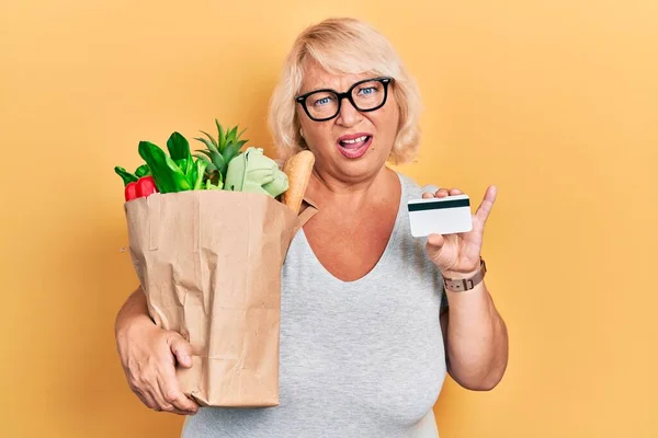 Medelålders Blond Kvinna Som Håller Livsmedel Och Kreditkort Chockansikte Ser — Stockfoto