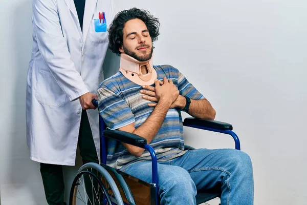 一个英俊的惊慌失措的男人坐在轮椅上 脖子上戴着项圈 双手放在胸前笑着 闭着眼睛 脸上挂着感激的手势 健康概念 — 图库照片