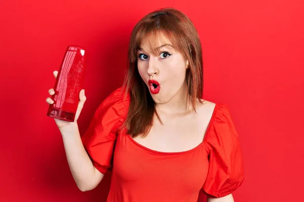 Redhead Young Woman Holding Shampoo Bottle Scared Amazed Open Mouth — Stock Photo, Image