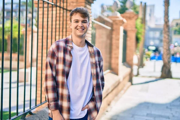 Genç beyaz adam gülümseyerek şehirde mutlu mesut duruyor..