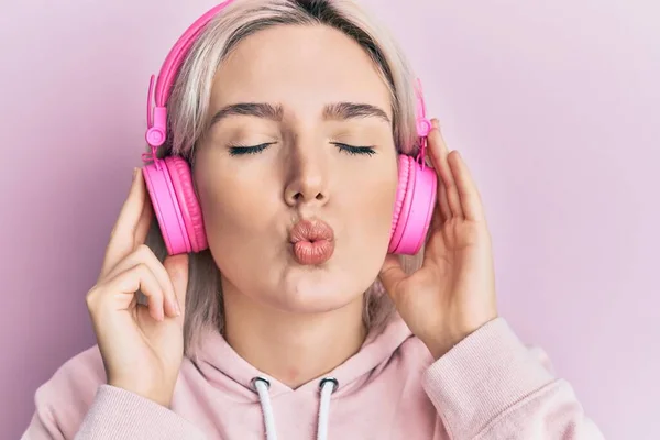 Joven Chica Rubia Escuchando Música Usando Auriculares Mirando Cámara Soplando — Foto de Stock