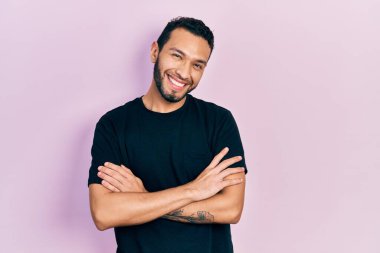 Siyah tişört giyen, kollarını kavuşturup kameraya gülümseyen İspanyol bir adam. pozitif kişi. 