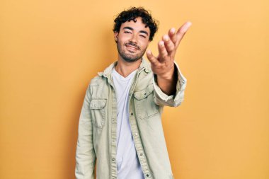 Gündelik kıyafetler giyen genç İspanyol adam dostça bir selamlama ve hoş geldin hediyesi olarak el sıkışmayı sunuyor. başarılı iş. 