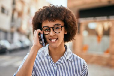 Genç İspanyol iş kadını gülümsüyor. Şehirdeki akıllı telefondan mutlu bir şekilde konuşuyor..