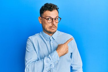 Gündelik kıyafet ve gözlük takan İspanyol genç adam endişeli ve gergin bir şekilde işaret ediyor. 