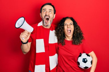 Orta yaşlı bir çift İspanyol kadın ve erkek eşarp takıp tezahürat oyunu oynuyorlar. Ellerinde megafon ve top tutuyorlar. Kızgın ve öfkeli çığlıklar atıyorlar.. 