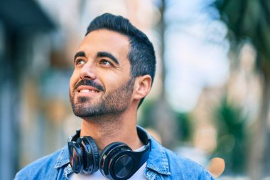 Şehirde kulaklık takarak mutlu gülümseyen genç İspanyol adam..