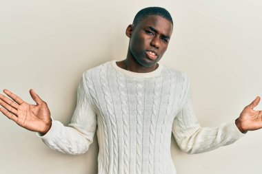 Sıradan kıyafetler giyen, kafası karışmış, elleri ve kolları havada genç Afro-Amerikalı bir adam. şüphe kavramı. 