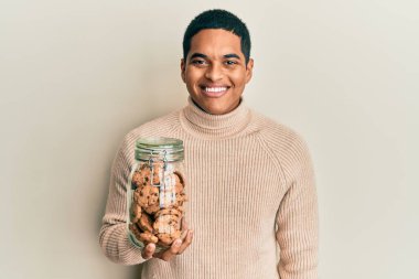 Genç, yakışıklı İspanyol adam elinde çikolata parçacıklı kurabiye kavanozu tutuyor. Olumlu ve mutlu görünüyor. Kendine güvenen bir gülümsemeyle dişlerini gösteriyor. 