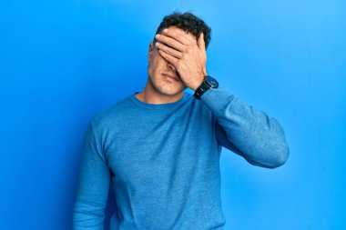 Latin kökenli genç adam, sıradan bir kazak giyip gözlerini eliyle kapatıyor, ciddi ve üzgün görünüyor. Görme, saklama ve reddetme konsepti 