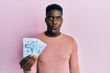 Yakışıklı siyah adam 50 Tayland baht banknotları tutuyor. Korkmuş ve şaşırmış bir şekilde ağzı açık, inançsız bir yüz. 