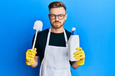 Genç kızıl saçlı adam tuvalet fırçasıyla ev işi yapıyor. Komik yüzlü yanakları şişiriyor. Ağzı havayla şişer, havayı yakalar.. 