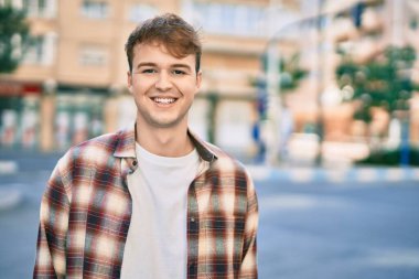 Genç beyaz adam gülümseyerek şehirde mutlu mesut duruyor..