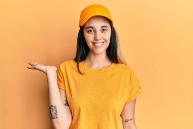 Teslimat üniforması giyen, şapkalı, neşeli gülümseyen, avuç içi kameraya bakan genç İspanyol kadın.. 