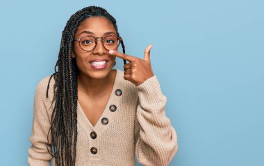 Afro-amerikan kadın, günlük kıyafetler giyip, el parmağı ve burunla işaret ederek, neşeyle gülümsüyor. güzellik konsepti 