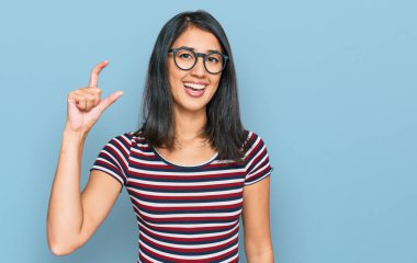 Güzel Asyalı genç bir kadın günlük kıyafetler ve gözlük takıyor gülümsüyor ve kendinden emin bir şekilde el hareketi yapıyor parmaklarıyla işaret yapıyor ve kameraya bakıyor. ölçüm kavramı. 