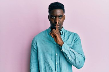 Yakışıklı, sıradan kıyafetler giyen, dudakları parmaklarıyla sessiz olmak isteyen siyahi bir adam. sessizlik ve gizli konsept. 