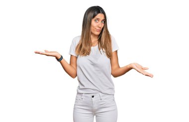 Sıradan beyaz tişört giyen, elleri ve kolları havada, kafası karışmış genç bir kadın. şüphe kavramı. 