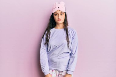 Yüzünde ciddi bir ifade olan uyku maskesi ve pijama giyen güzel bir ortadoğulu kadın. Basit ve doğal bir şekilde kameraya bakıyorsun.. 