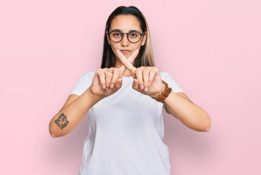 Gündelik beyaz tişört giyen genç İspanyol kadın. Reddedilmiş yüz ifadesi. Eksi işareti yapan parmaklar. 