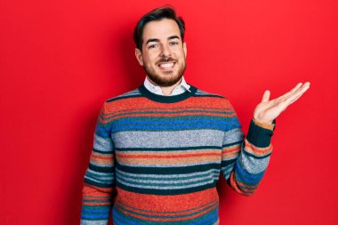 Sakallı, zarif yün süveter giyen, neşeli gülümseyen, eli kameraya bakan yakışıklı beyaz adam.. 