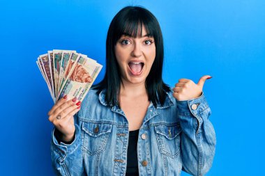 Genç İspanyol kadın elinde Mısırlı banknotlar tutarken başparmağını yana uzatıyor ve ağzı açık gülümsüyor. 
