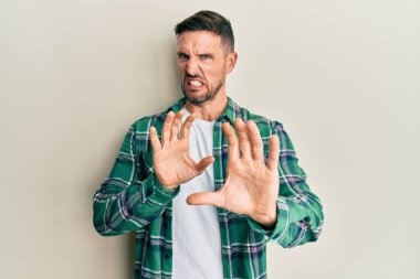 Sakallı yakışıklı, sıradan kıyafetler giyen, tiksindirici ve tiksindirici bir yüz ifadesi takınan, tiksindirici bir adam. Eller havada. 