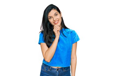 Günlük kıyafetler giyen genç İspanyol kadın kameraya kendinden emin bakıyor kollarını kavuşturup gülümseyerek ve çenesini kaldırarak. Olumlu düşünmek. 