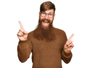 Genç İrlandalı kızıl elbiseli ve gözlüklü adam farklı yönleri gösteren kendine güvenen bir şekilde gülümsüyor. reklam için kopyalama alanı 