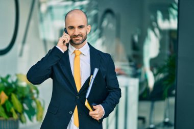 Genç Latin kökenli kel iş adamı gülümsüyor. Şehirdeki akıllı telefondan mutlu bir şekilde konuşuyor..